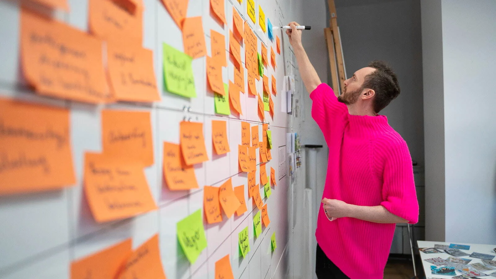 Person notiert an einer Wand voller orangefarbener und grüner Klebezettel während eines Strategie-Workshops