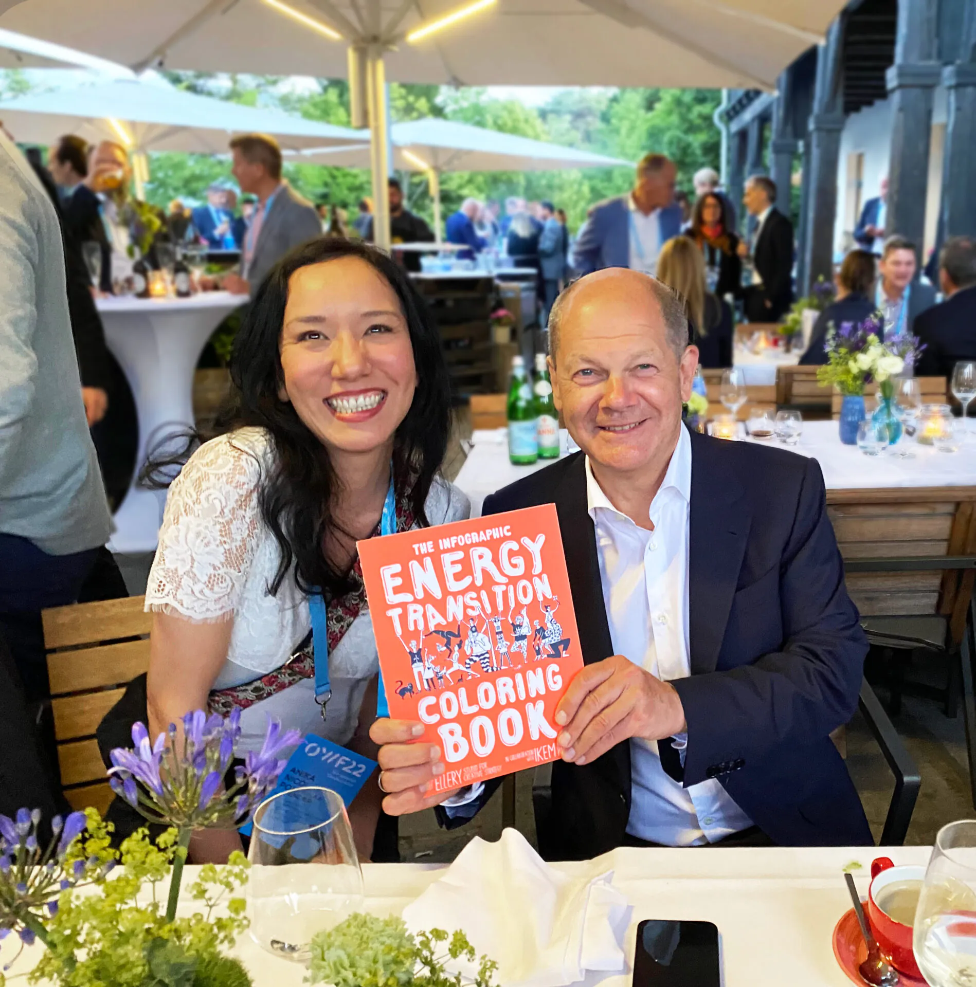 Zwei Personen halten bei einer Abendveranstaltung das Infographic Energy Transition Coloring Book von Ellery Studio in die Kamera