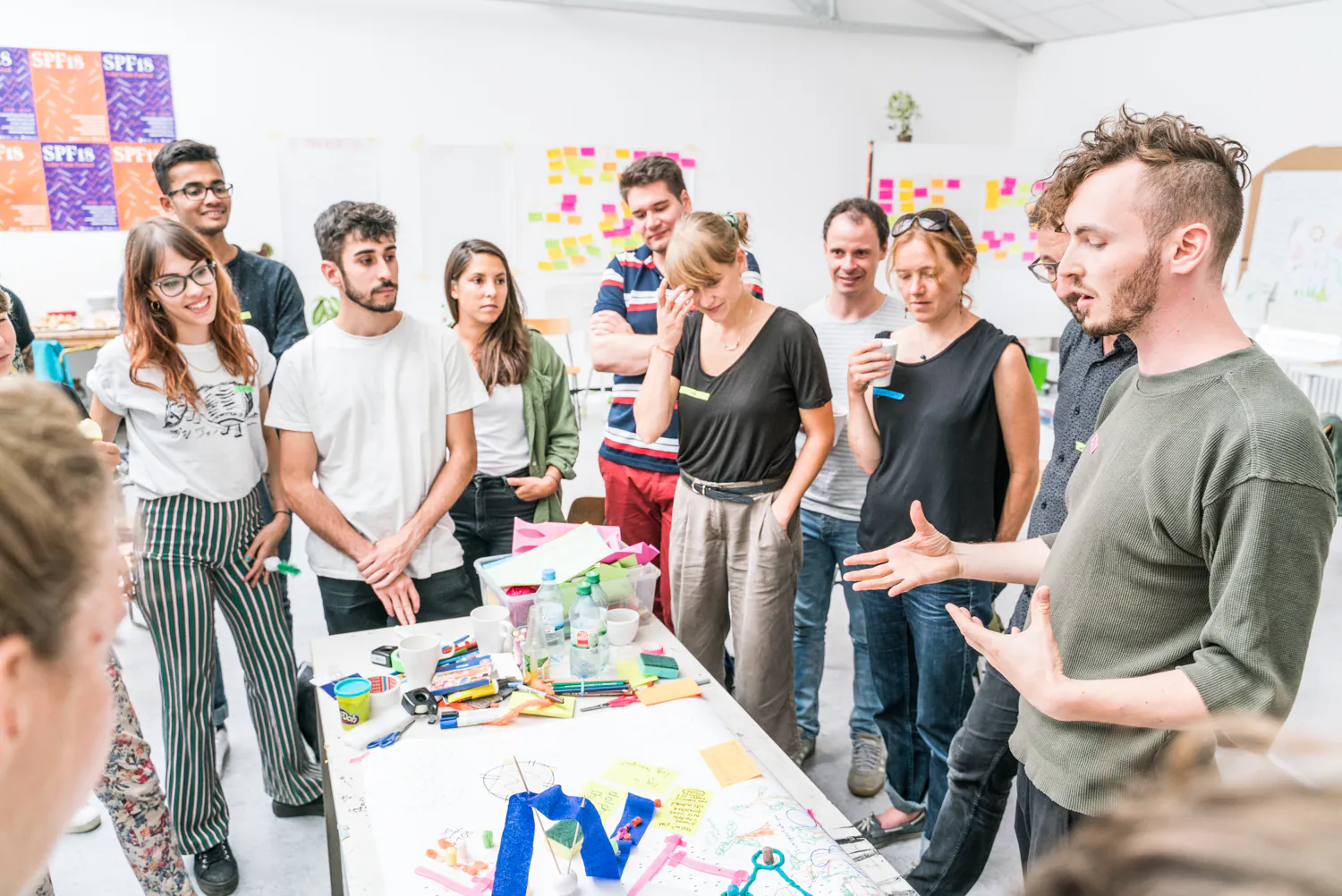 Workshop-Teilnehmende stehen um einen Tisch mit Bastelmaterial und diskutieren mit einem Moderator